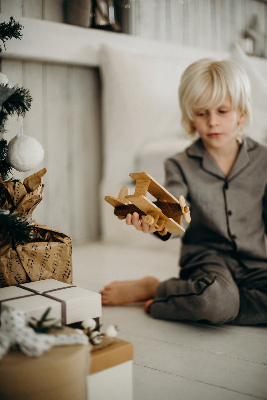 boy in gray pajamas holding brown wooden plane toy