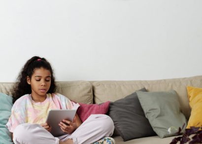 photo of girl sitting on sofa while using tablet