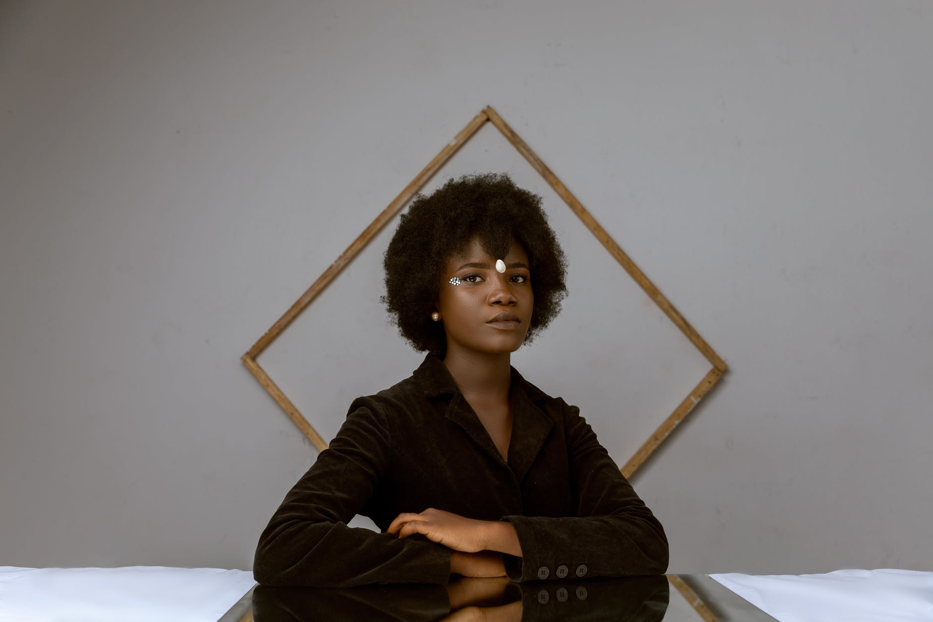 elegant young black woman with afro hair resting in room near decorated wall with frame