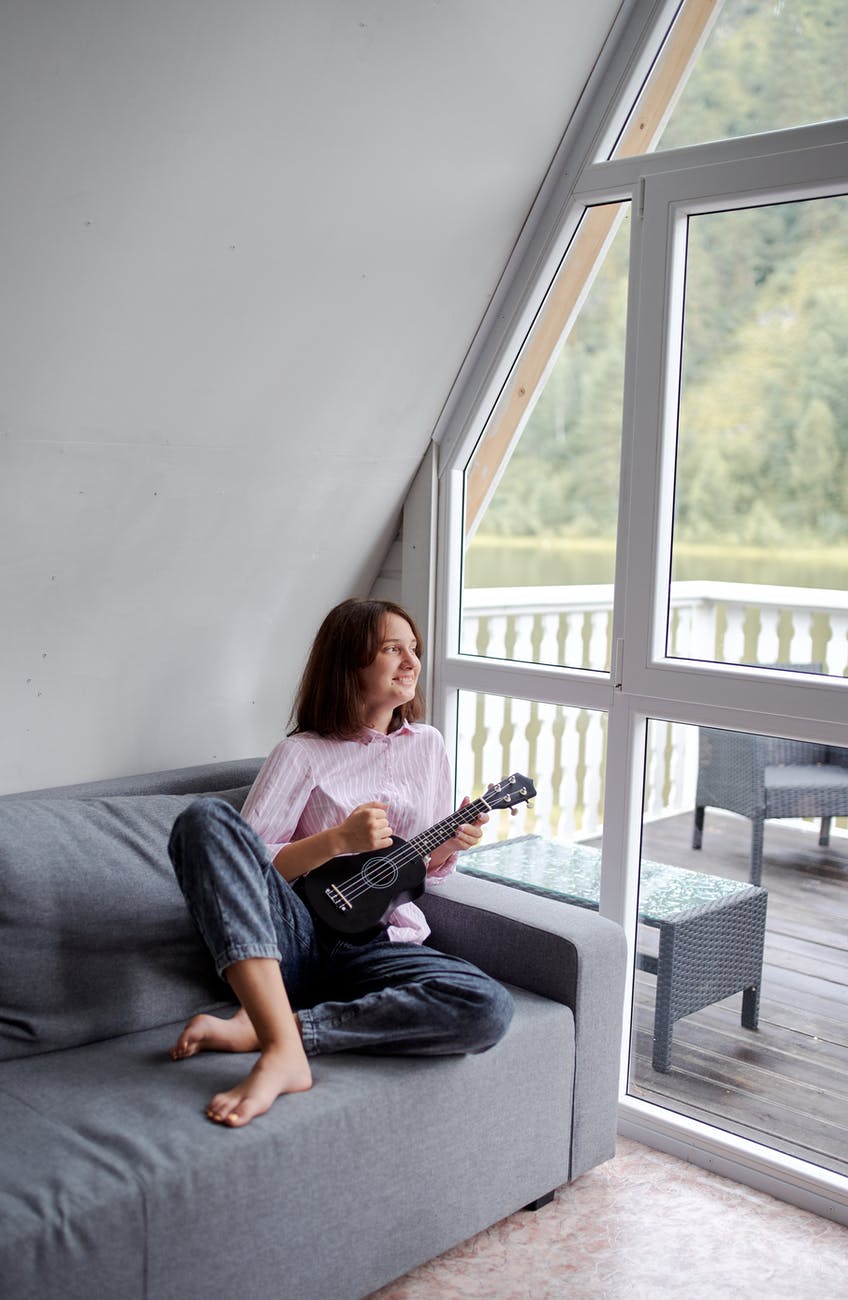 smiling woman playing ukulele on couch in countryside house